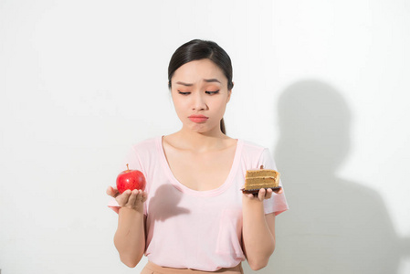 女人手捧着蛋糕中的甜和苹果的果子选择, 试图抗拒诱惑, 做出正确的饮食选择。减肥饮食困境暴食概念
