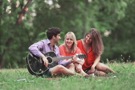 在城市公园的草地上坐着吉他的学生组