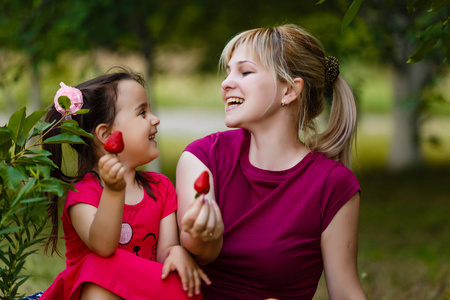 夏日快乐母亲的肖像和她的小女儿在绿色美丽的公园草莓