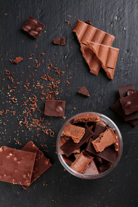 黑色和牛奶巧克力棒和碎片在黑色的一块一块一块。甜食和甜点的概念。食品背景顶部视图