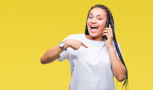 年轻的编织头发非洲裔美国女孩显示打电话使用智能手机在孤立的背景与惊喜的脸指向自己