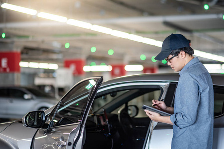 年轻的亚洲汽车技工持有数字平板检查汽车门在汽车服务车库。机械维修工程师在汽车行业工作。汽车维修理念