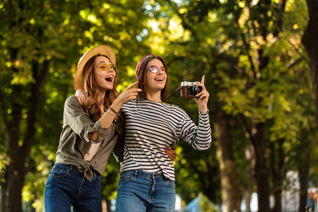 图像的兴奋漂亮的年轻快乐的妇女朋友走在户外与背包和相机指点
