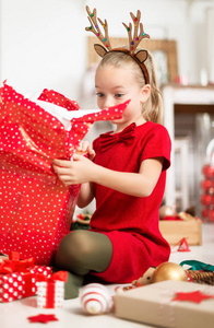 可爱的超级兴奋的年轻女孩打开大红色圣诞礼物, 而坐在客厅的地板上。坦诚的家庭圣诞节时光生活方式背景