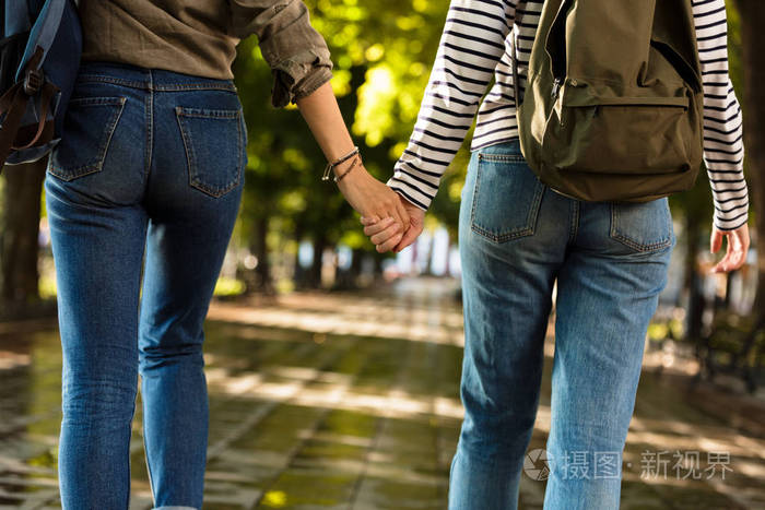 年轻女性朋友的裁剪照片在户外与背包牵手彼此