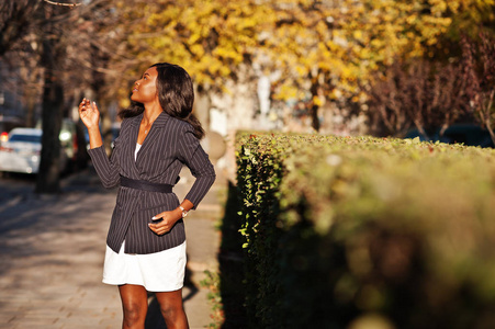 成功时尚的非洲裔美国妇女在夹克和裙子摆在阳光明媚的秋天天在街上