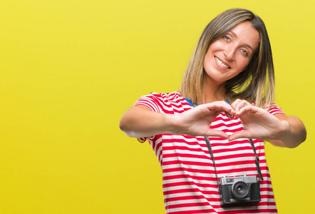 年轻美丽的女人拍照使用老式照片相机在孤立的背景下微笑的爱显示心脏的符号和形状与手。浪漫理念