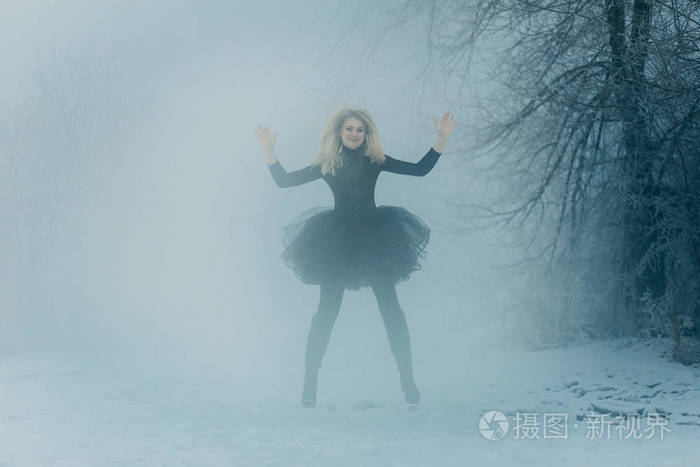 一个穿着黑色连衣裙的年轻女子在朦胧的冬日森林中跳跃