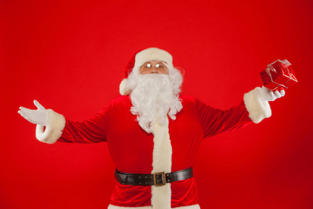 圣诞老人戴着礼品盒的手戴手套的照片, 在一个红色的背景图上