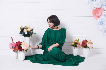 褐发女郎妇女在丝绸绿色的礼服坐在一个光背景摆着花
