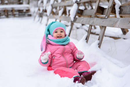 穿着粉色连身衣的小女孩走在雪天公园里