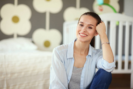 年轻的女人坐在儿童床边的地板上。年轻的妈妈