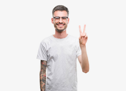 年轻的纹身成年男子微笑着看着相机显示手指做胜利标志。第二个
