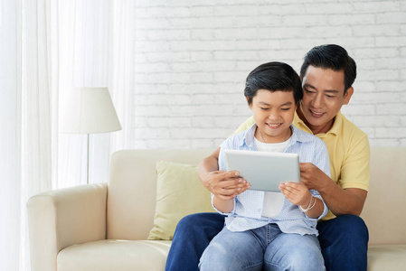 亚洲爸爸和小儿子在家里的沙发上玩电脑游戏数码片
