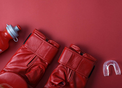 红色皮革拳击手套, 一个塑料水瓶和硅胶帽的牙齿上的红色背景, 复制空间