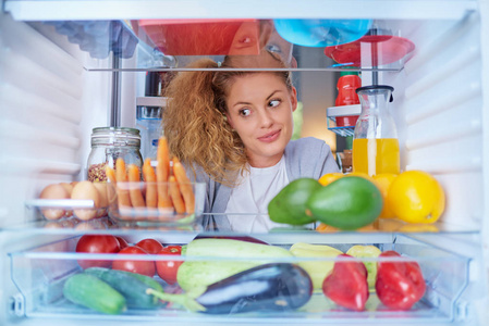 一个女人站在冰箱前, 装满了杂货, 看着吃的东西。从冰箱内部拍摄的照片