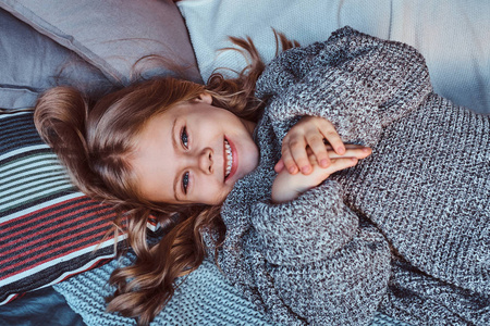 一个小女孩的特写肖像躺在床上的保暖毛衣