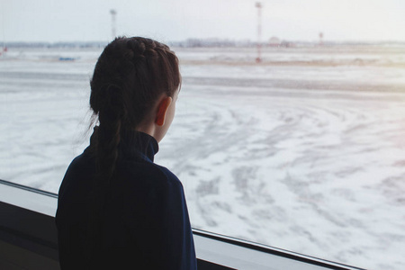 儿童女孩在机场附近的窗口看着飞机, 等待飞行时间照片