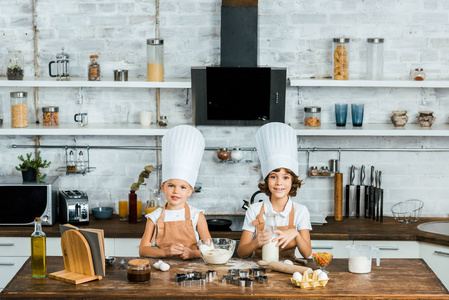 可爱的孩子在厨师帽和围裙准备面团为曲奇饼和微笑在照相机