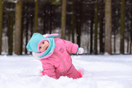 穿着粉色连身衣的小女孩走在雪天公园里