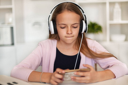 听音乐的年轻女孩在她的电话和白色耳机被技术吸收的青少年的画像