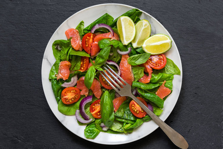 三文鱼沙拉配菠菜樱桃西红柿红洋葱和罗勒, 白色大理石板配叉子。健康食品概念。顶部视图