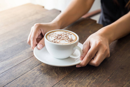 手持白色杯咖啡的女子手紧贴木桌上的美丽图案艺术