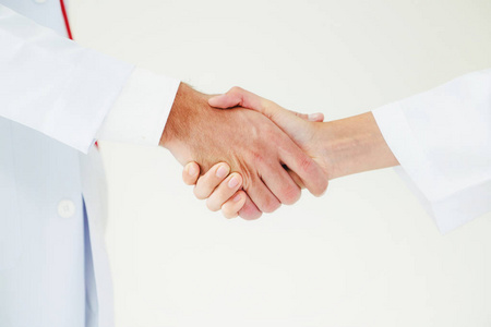 医生在白色背景下, 与另一位医生握手, 展示了专业医护人员的成功和团队精神。接近医生的手
