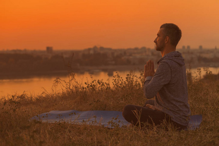 男子在日落时做瑜伽与城市的看法, 帕德马萨纳马莲花的位置。色调的图像