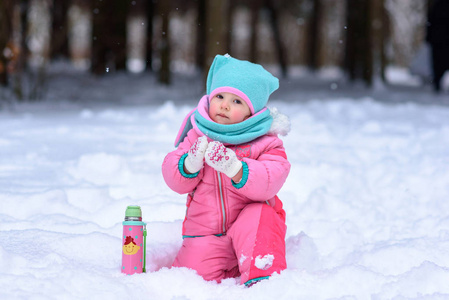 穿着粉色连身衣的小女孩走在雪天公园里