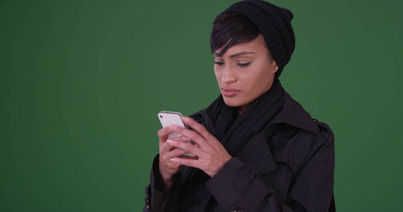 穿着黑色大衣的时尚女性在绿屏上的手机上发短信