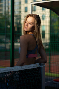迷人的金发女孩与完美的身体穿着运动服装摆在网球场上