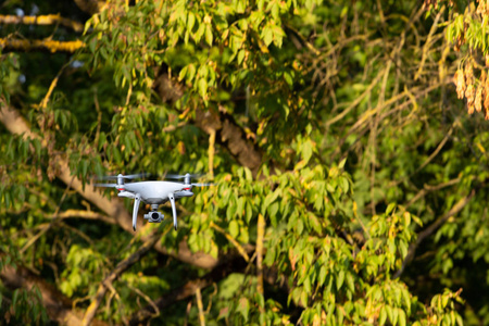 白色飞行无人机与照相机在绿色树背景 quadrocopter
