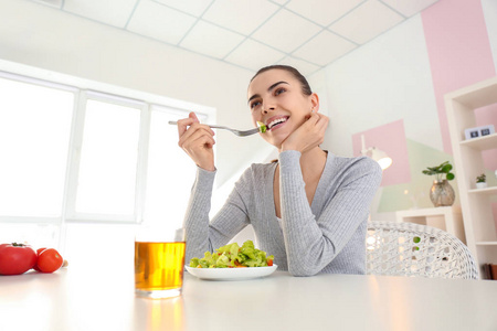 年轻的妇女在家里吃新鲜的沙拉。健康食品概念