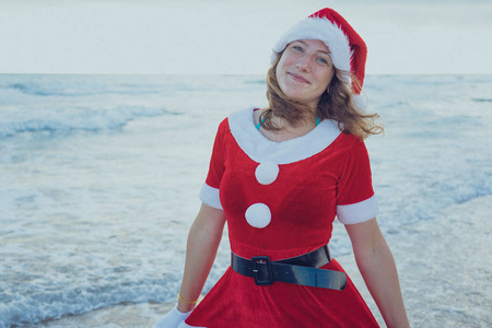 女孩装扮成圣诞老人站在海滩或海洋。圣诞节旅程的概念。新年快乐, 圣诞愉快