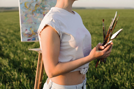画家的年轻女孩站着, 拿着画笔画画。一个与自然