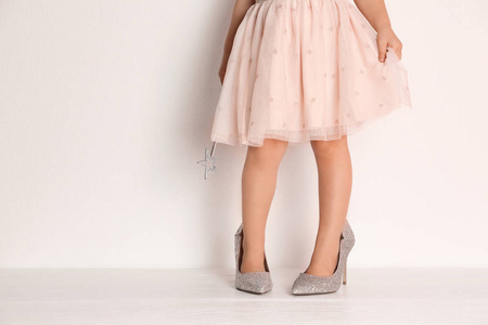 小女孩在超大号的鞋子在白色墙壁附近与空间为文本, 特写在腿