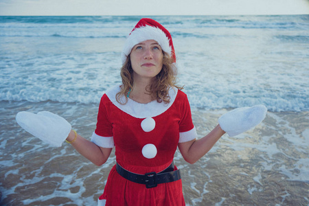 女孩装扮成圣诞老人站在海滩或海洋。圣诞节旅程的概念。新年快乐, 圣诞愉快