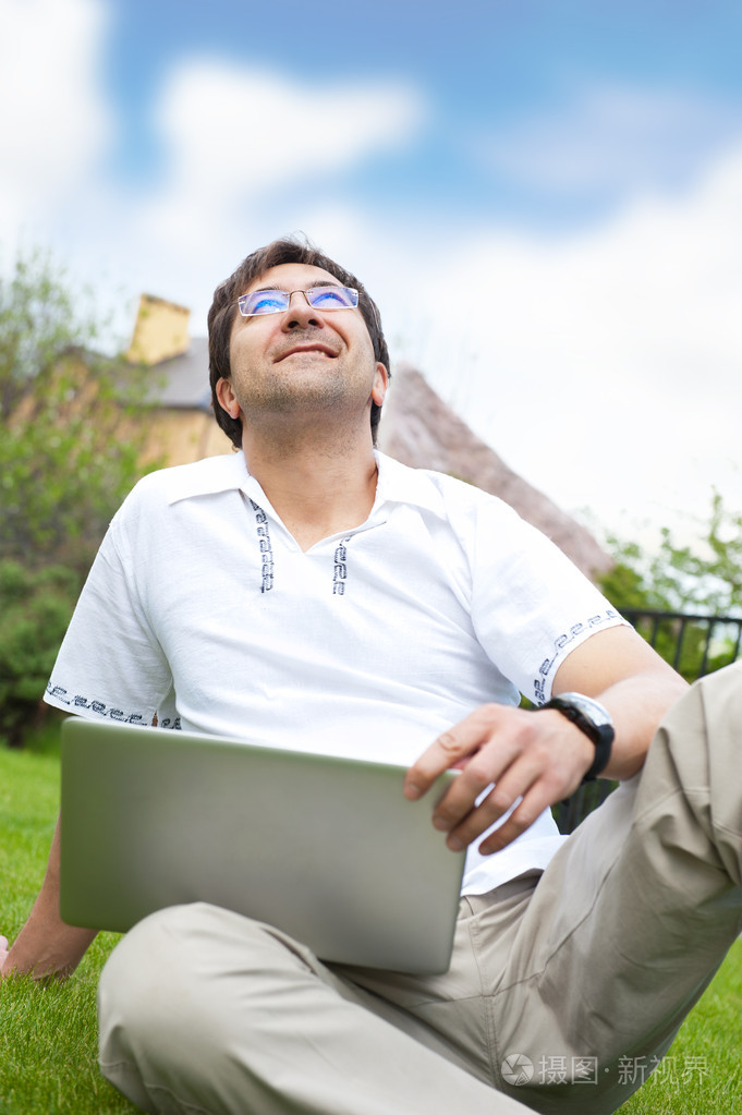 笔记本电脑室外坐在他的后院和仰望天空微笑着男人