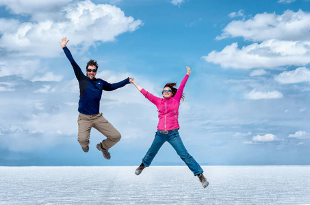 快乐的情侣跳在乌尤尼盐公寓反对多云的天空, 玻利维亚, 南美