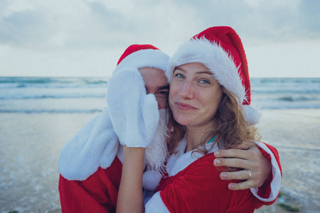 快乐的情侣在海滩上漫步圣诞老人的服装。圣诞节假期的概念