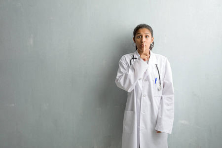 年轻的印度医生妇女对墙壁保守秘密或要求沉默, 严肃的面孔, 服从概念