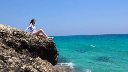 有魅力的女人坐在石头附近的水。美丽的女人坐在岩石附近的海边