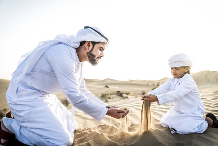 快乐的家庭玩在迪拜的沙漠嬉戏的父亲和他的儿子在户外乐趣