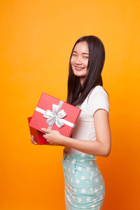 年轻的亚洲妇女打开一个礼品盒在明亮的黄色背景