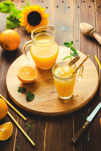一杯鲜榨的橙汁, 上面放着冰块和橘子在木桌上。秋天舒适质朴的心境静物