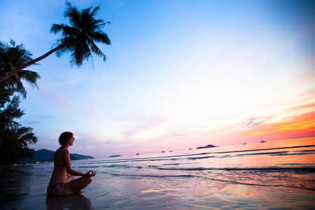 美丽的女人做莲花瑜伽姿势附近海洋沙滩上的日落时在泰国