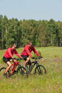 年轻夫妇骑山地自行车在春天草甸