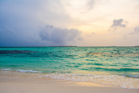 在马尔代夫岛沙质海滩与色彩斑斓的天空和浪的大海上空的云块戏剧性的美丽的日落景观