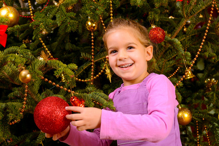 可爱的蹒跚学步的女孩举行装饰圣诞玩具球
